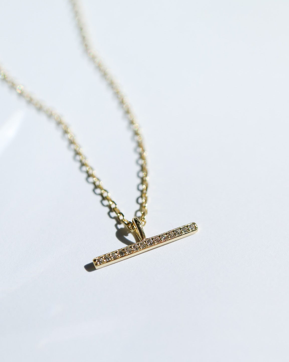 Gold necklace with a bar pendant on a white background