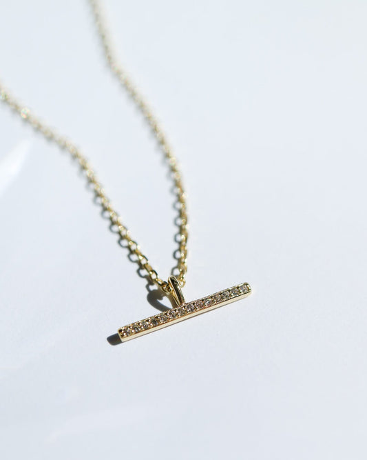 Gold necklace with a bar pendant on a white background