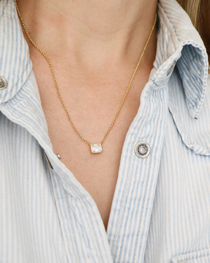 Necklace with a square pendant worn by a person in a light blue striped shirt.