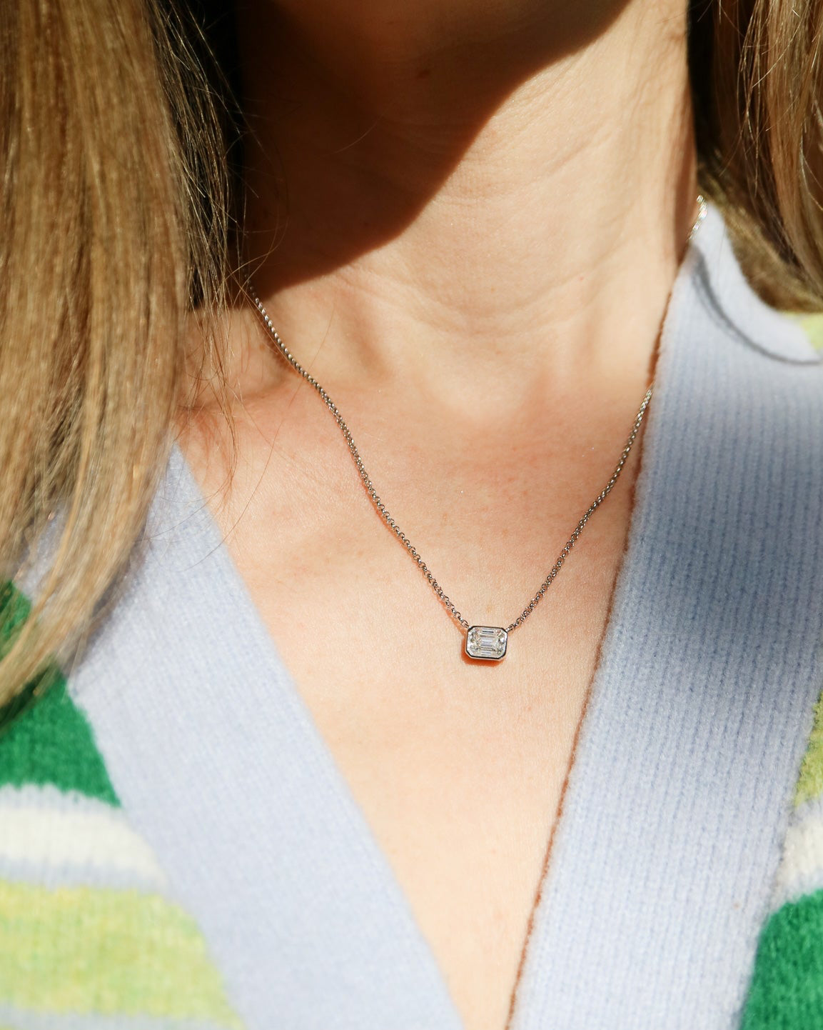 Necklace with a small pendant worn by a person in a green and white striped sweater.