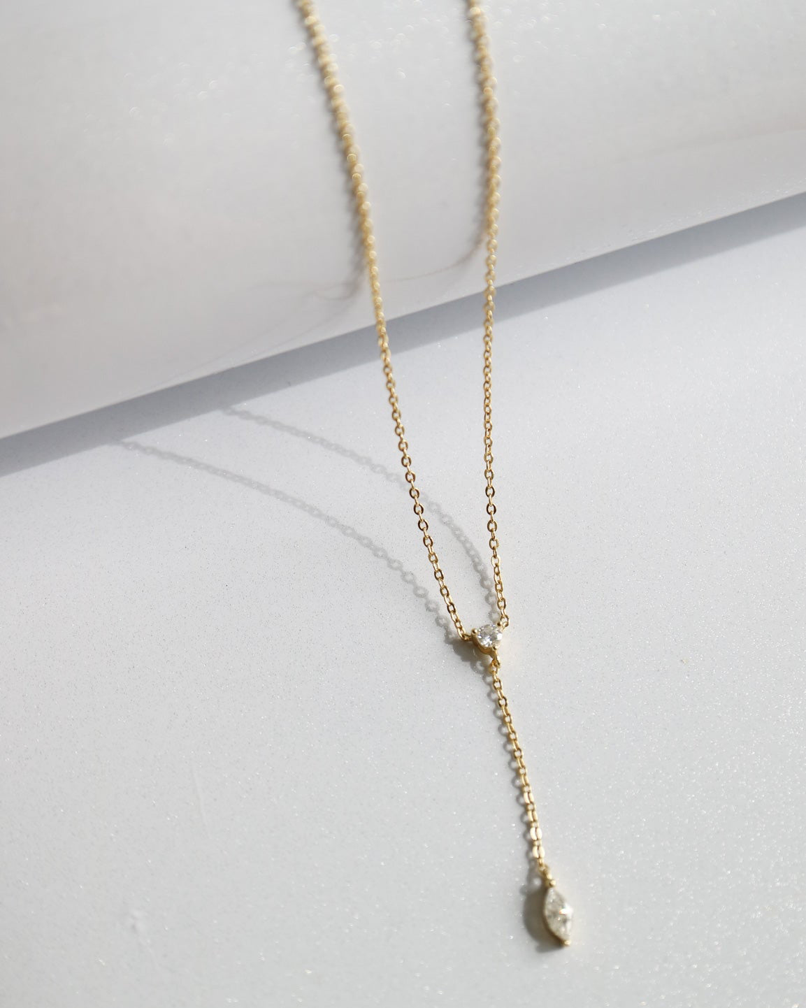 Gold necklace with a small pendant on a light gray surface