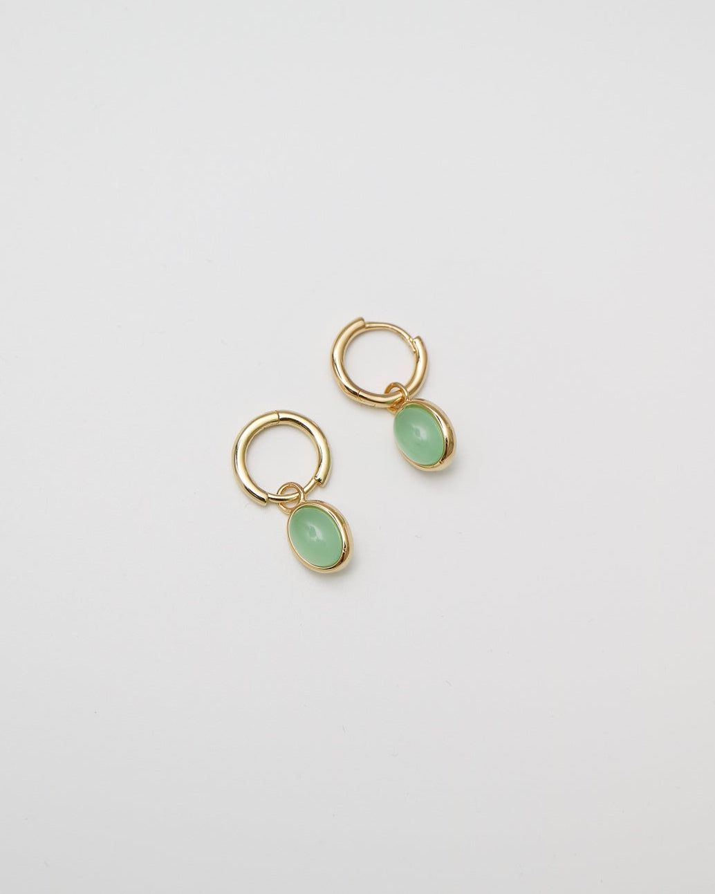 Gold earrings with green gemstones on a light gray background