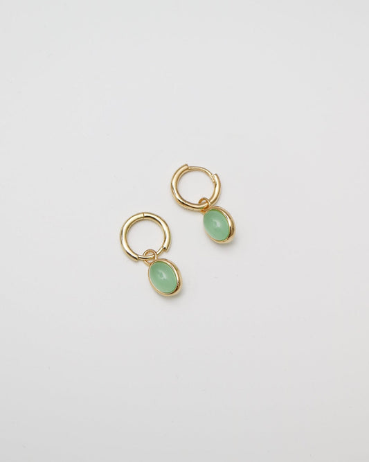 Gold earrings with green gemstones on a light gray background