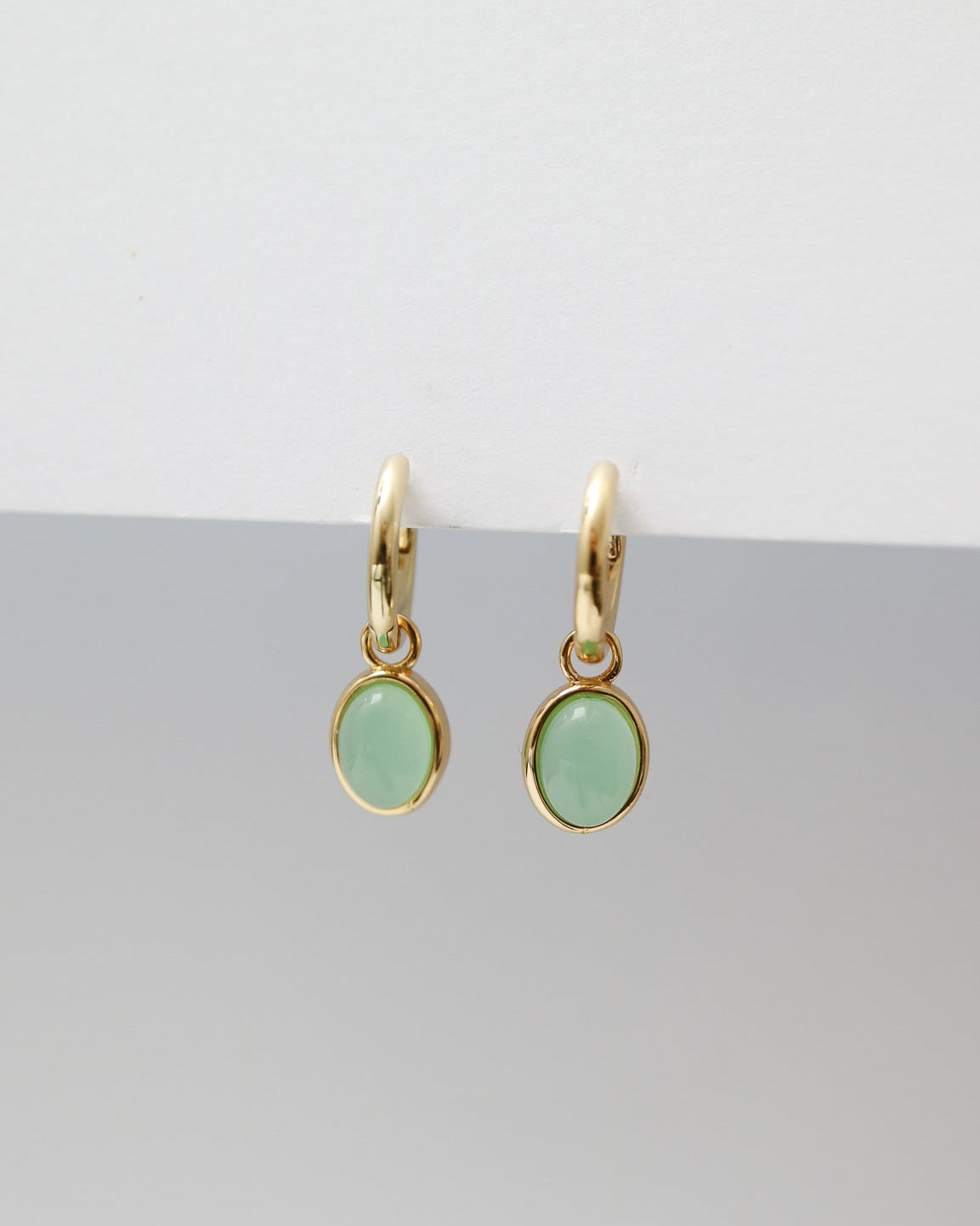 Gold earrings with green gemstones on a gray background