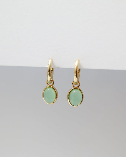 Gold earrings with green gemstones on a gray background