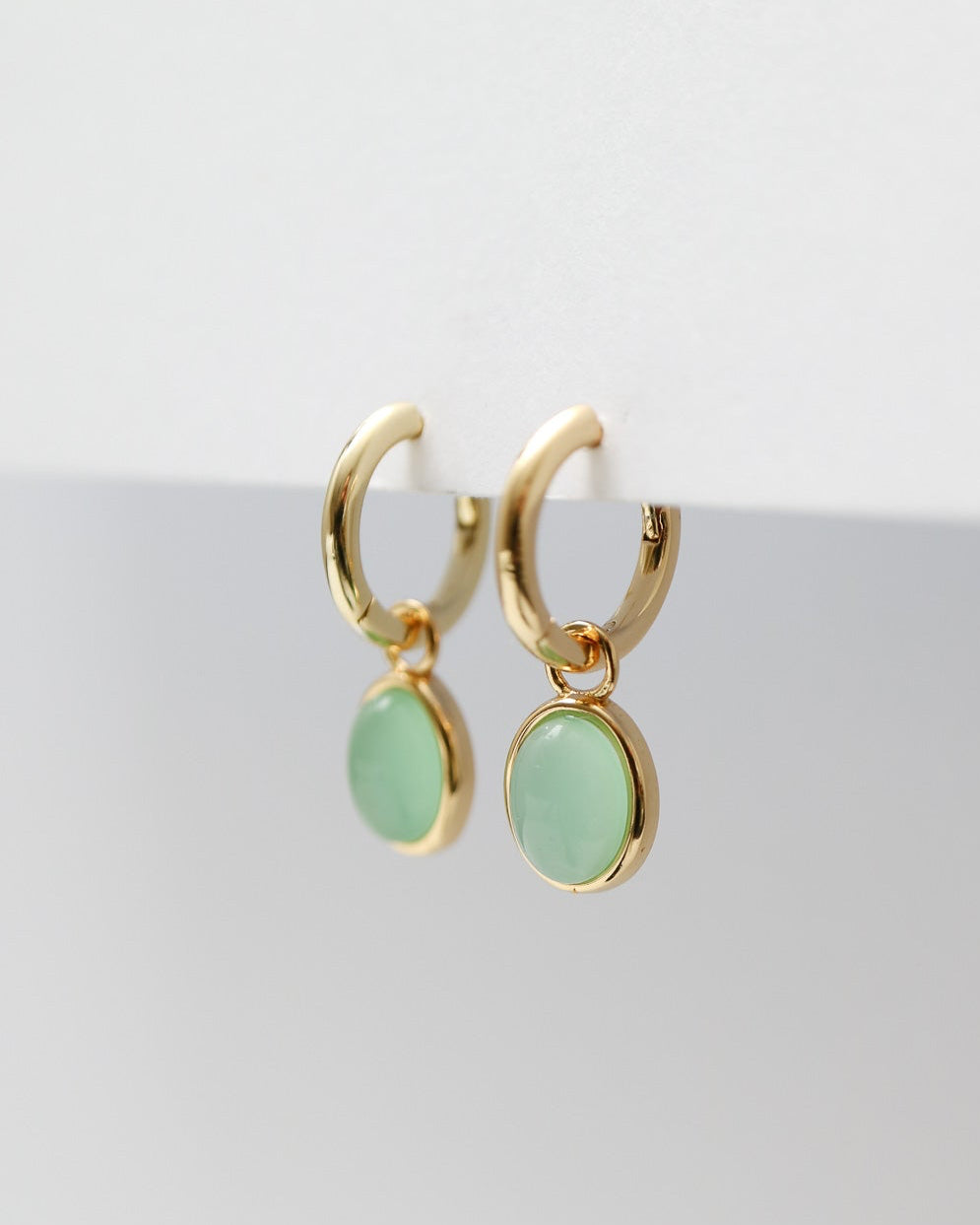 Gold hoop earrings with green gemstones on a white background