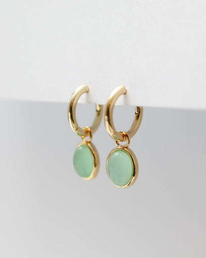 Gold hoop earrings with green gemstones on a white background