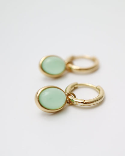 Gold hoop earrings with green round stones on a light gray background