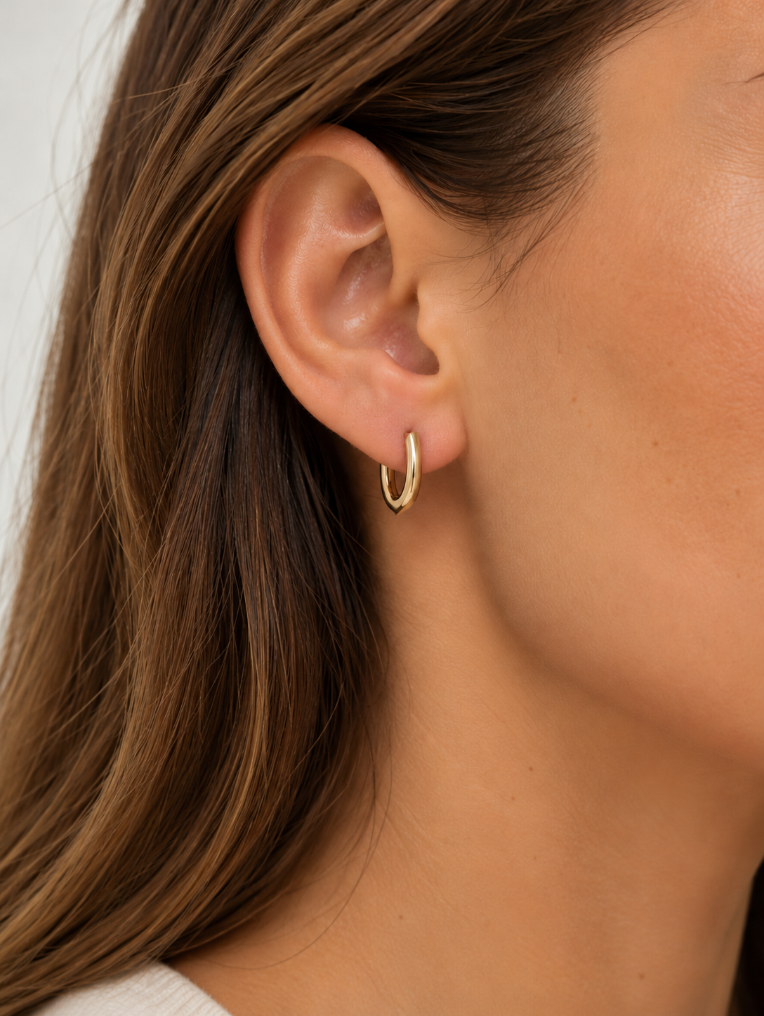 9kt solid gold Rounded V-Shaped Huggie Earrings featuring a polished finish, rounded silhouette and subtle V-shaped base, photographed on a woman's ear.