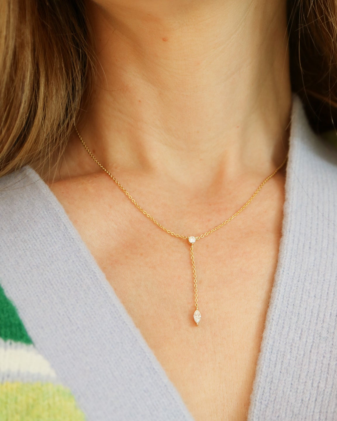 Close-up of a gold necklace worn by a person with a light gray cardigan and green striped garment.