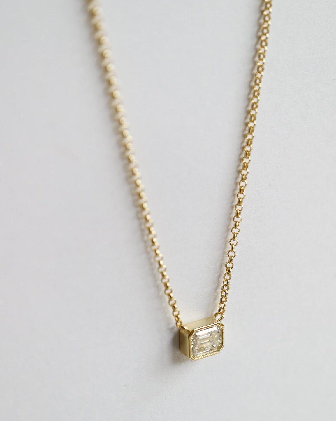 Gold necklace with a square pendant on a light gray background