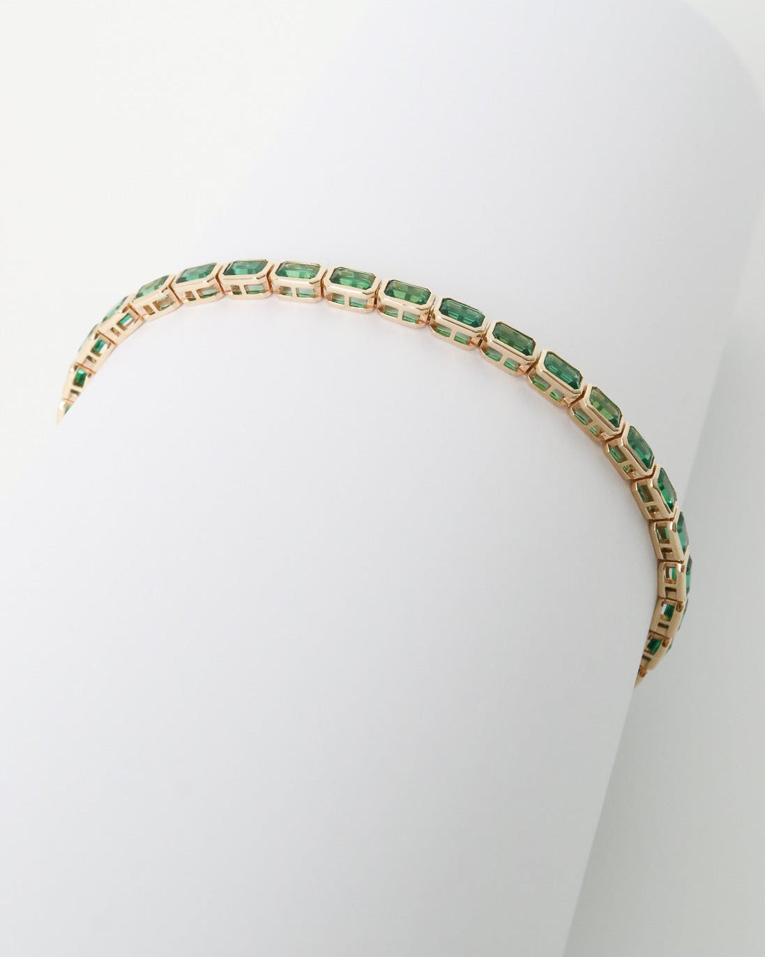Gold bracelet with green gemstones on a white background