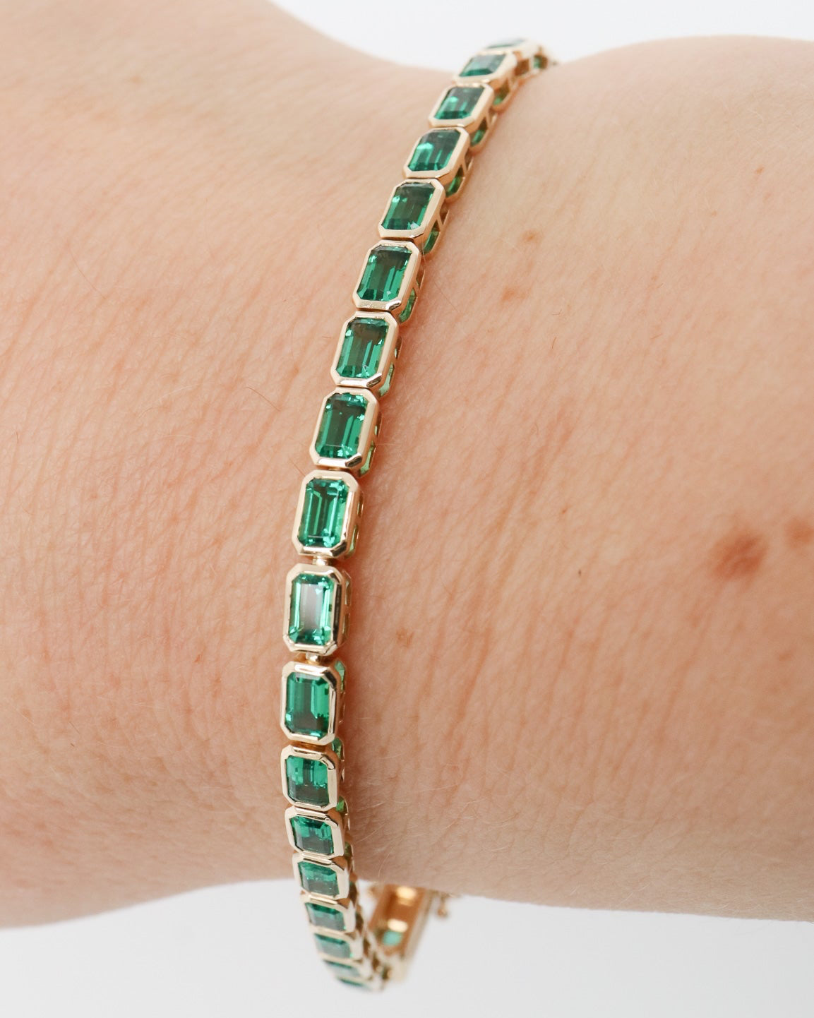 Gold bracelet with green gemstones on a wrist against a white background