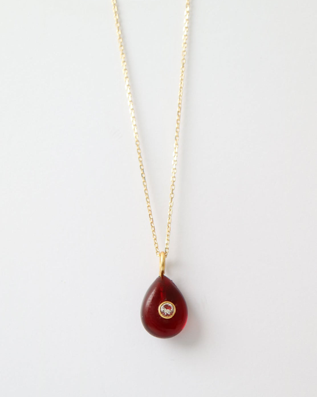 Garnet Glow Pendant featuring a deep red teardrop gemstone with a bezel-set cubic clear quartz and gold plated sterling silver bail on a white background.