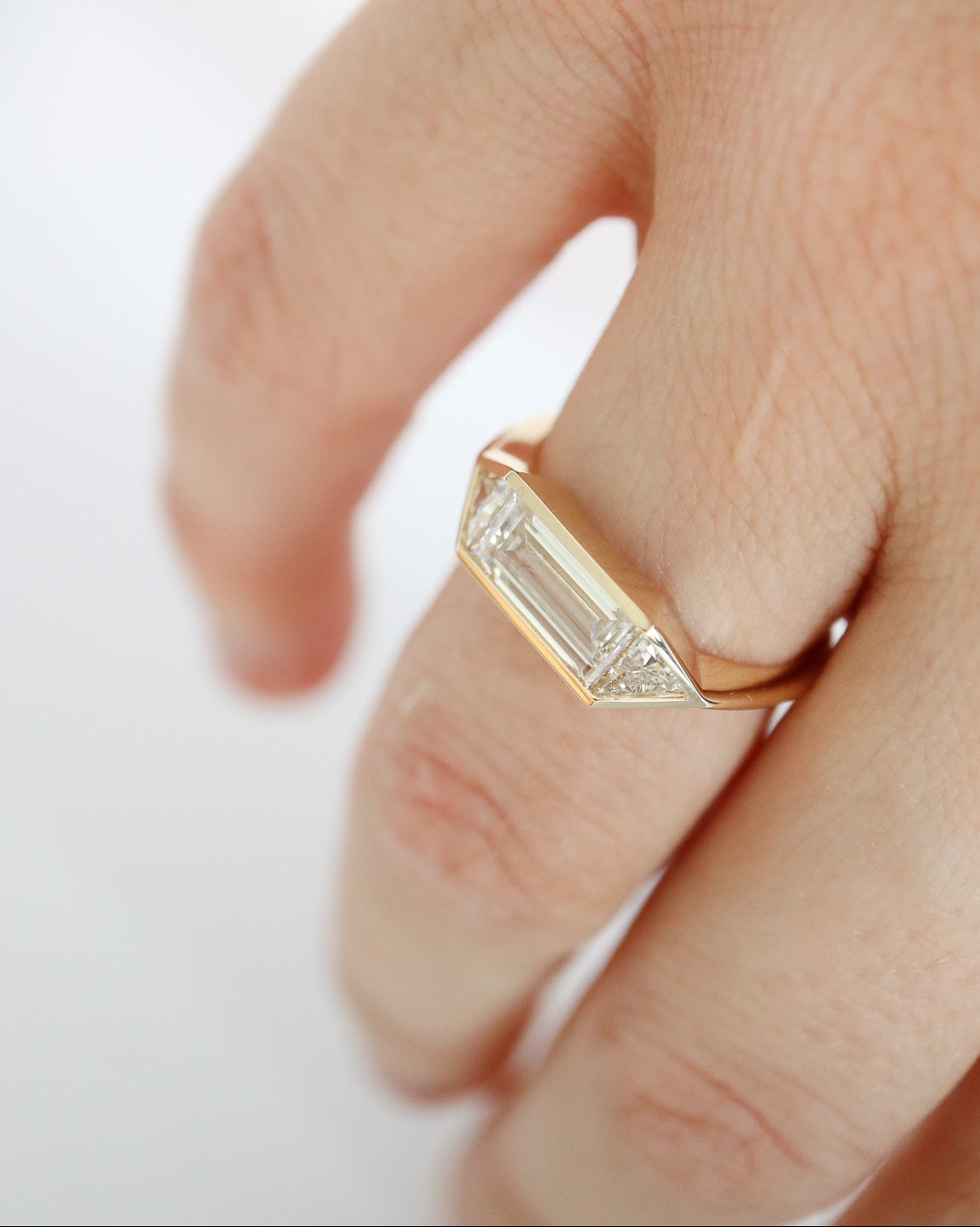 Gold ring with a diamond on a finger against a white background