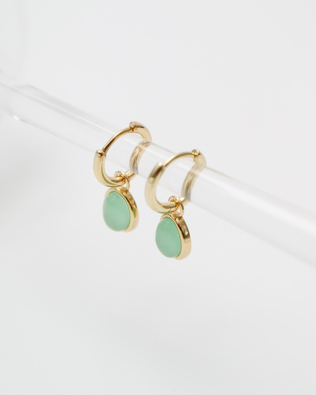 Gold hoop earrings with green teardrop charms on a white background