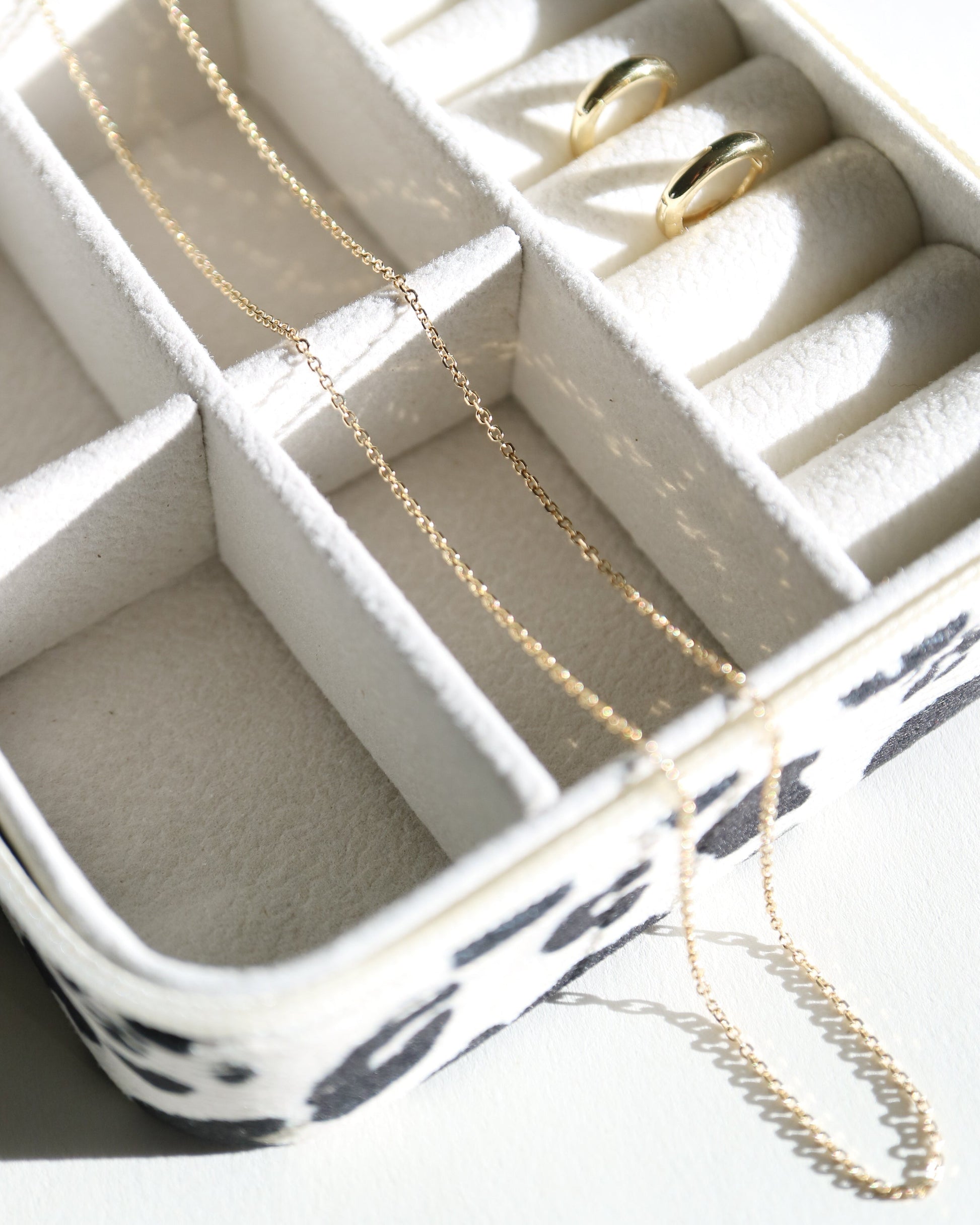 Jewelry organizer with gold necklaces and rings on a white surface