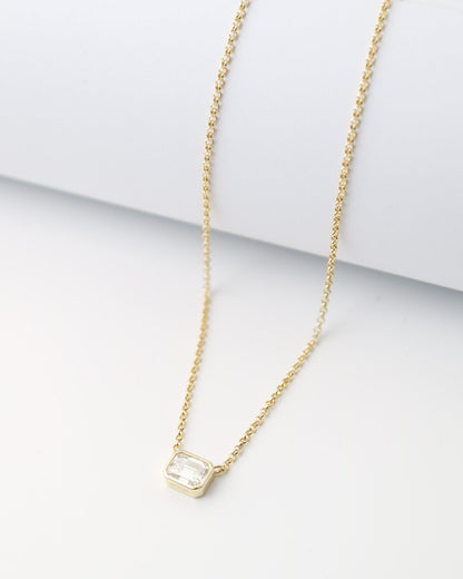 Gold necklace with a small pendant on a white surface