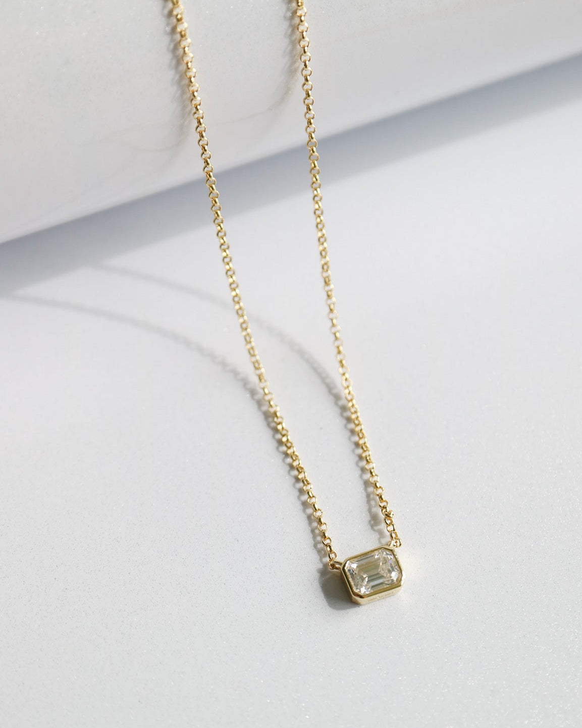 Gold necklace with a green gemstone pendant on a light gray background