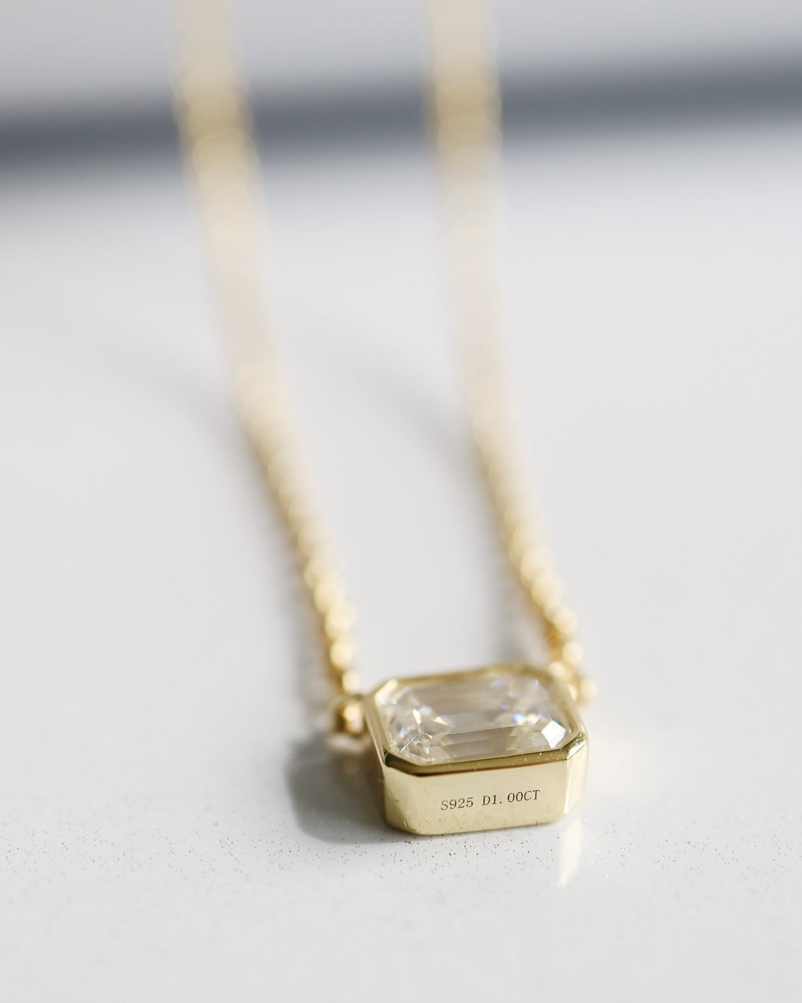 Gold necklace with a clear gemstone pendant on a light gray background