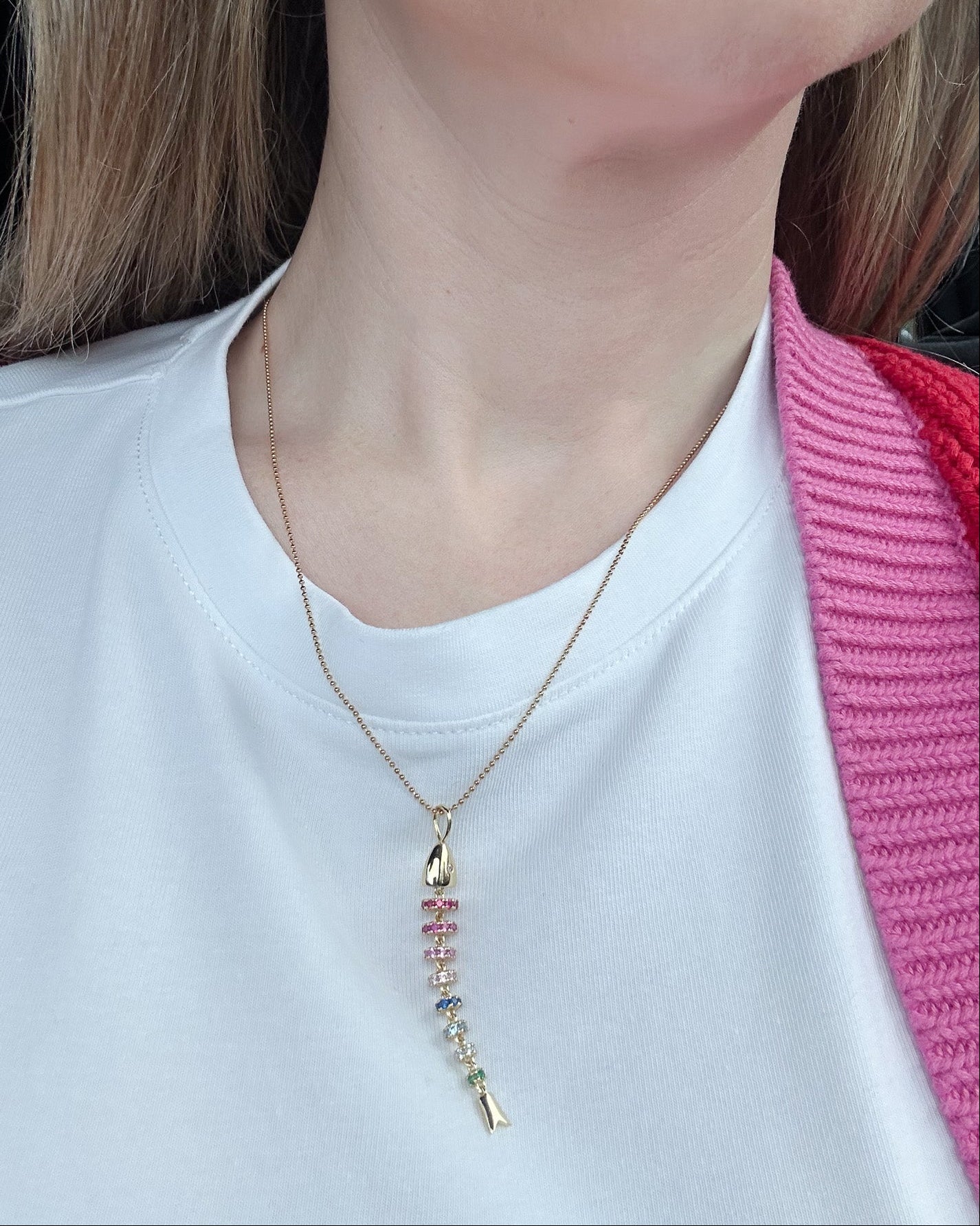 Person wearing a gold necklace with colorful beads on a plain background