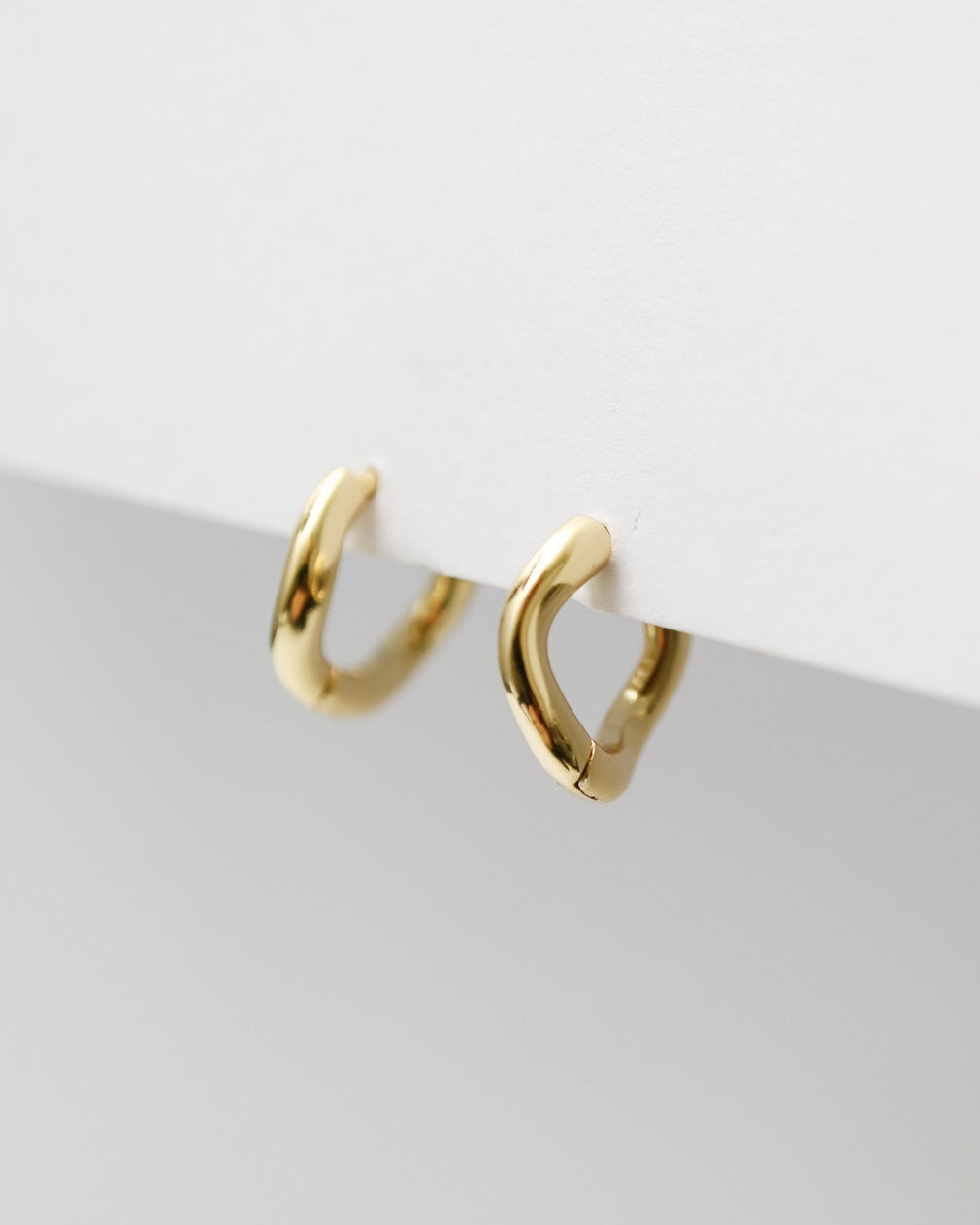 Gold hoop earrings on a light gray surface with a white background