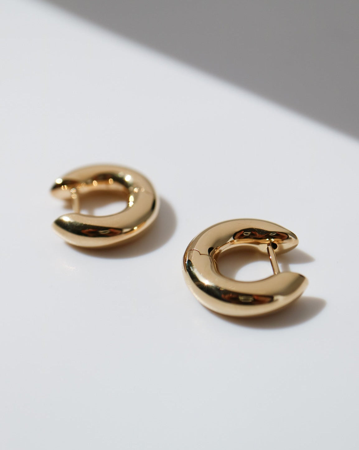 Gold hoop earrings on a white surface with a gray background