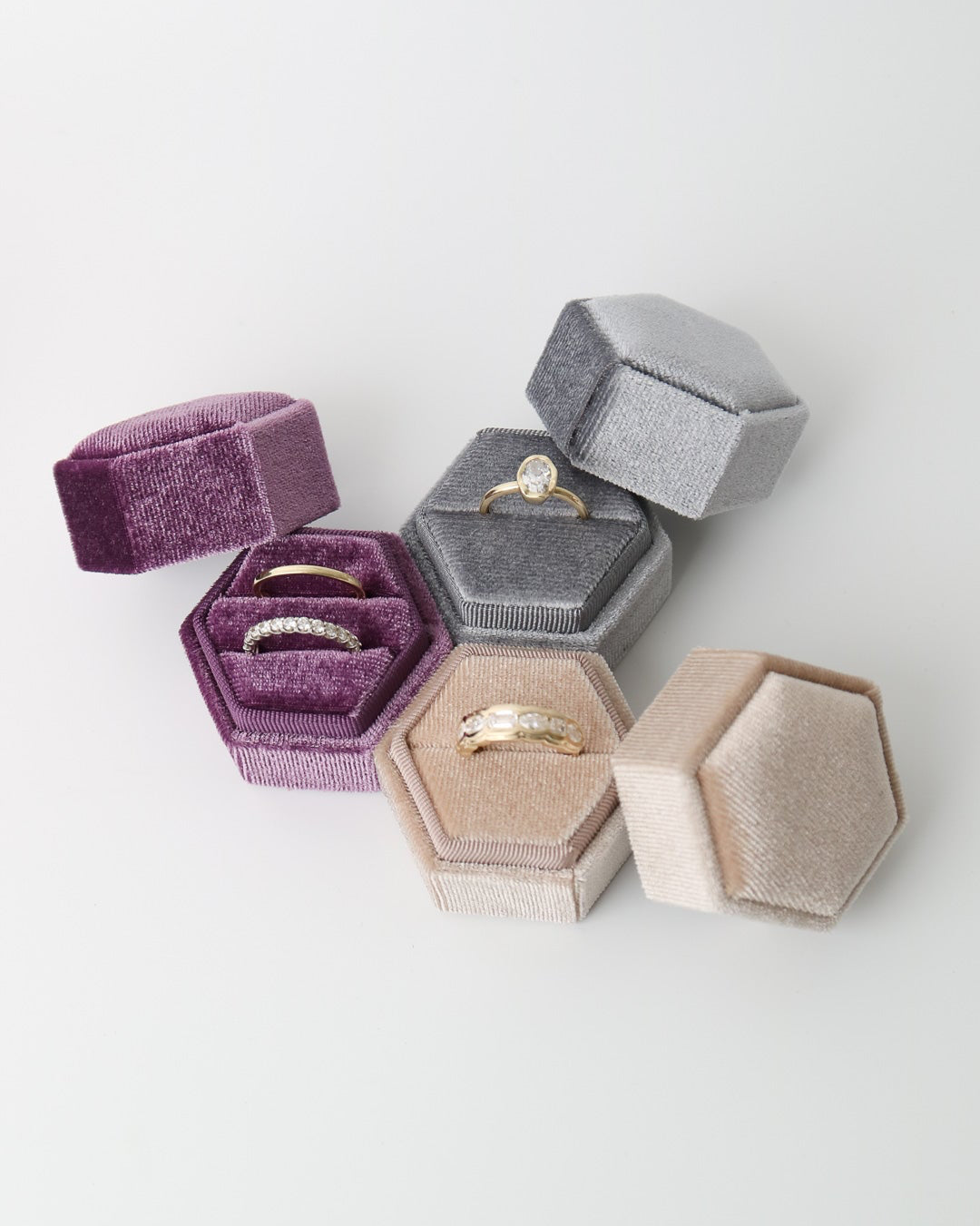 Hexagonal jewelry boxes in various colors with rings inside on a light background