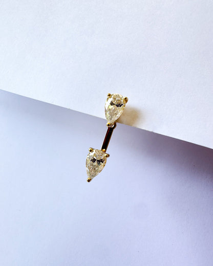 A gold-plated barbell stud earring featuring two pear-cut clear gemstones, photographed against a clean white background.