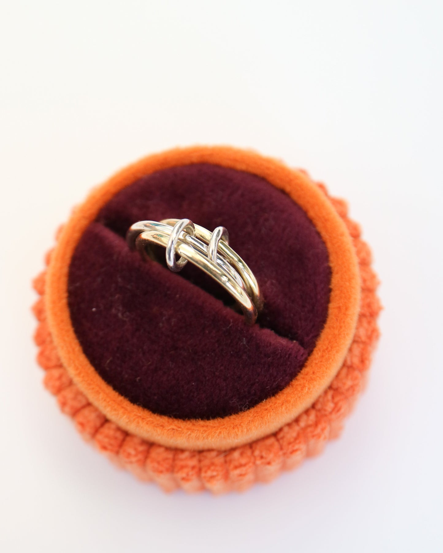 Gold ring on a round orange and red velvet jewelry box against a white background