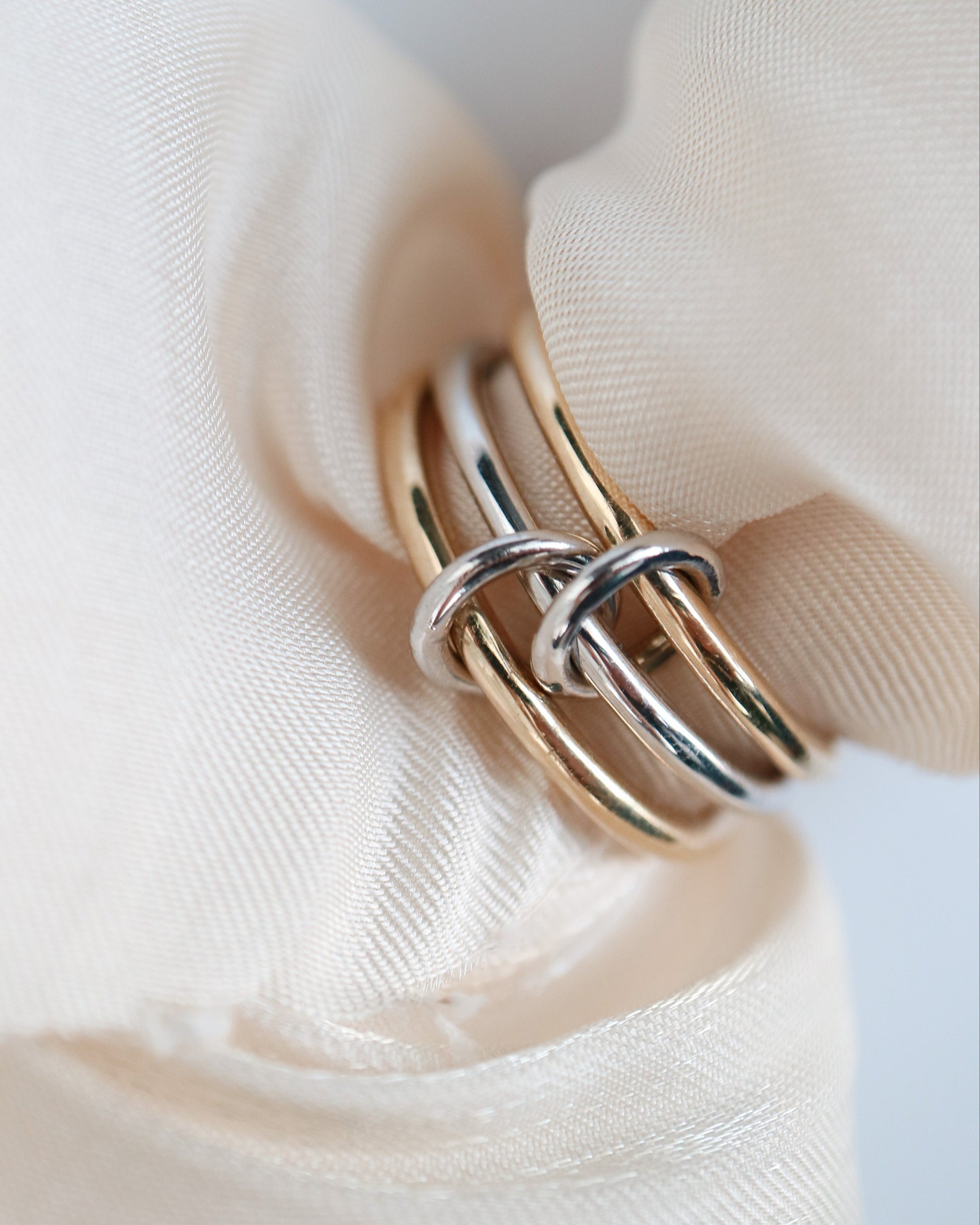 Three interlocking 9ct gold rings on a beige fabric background