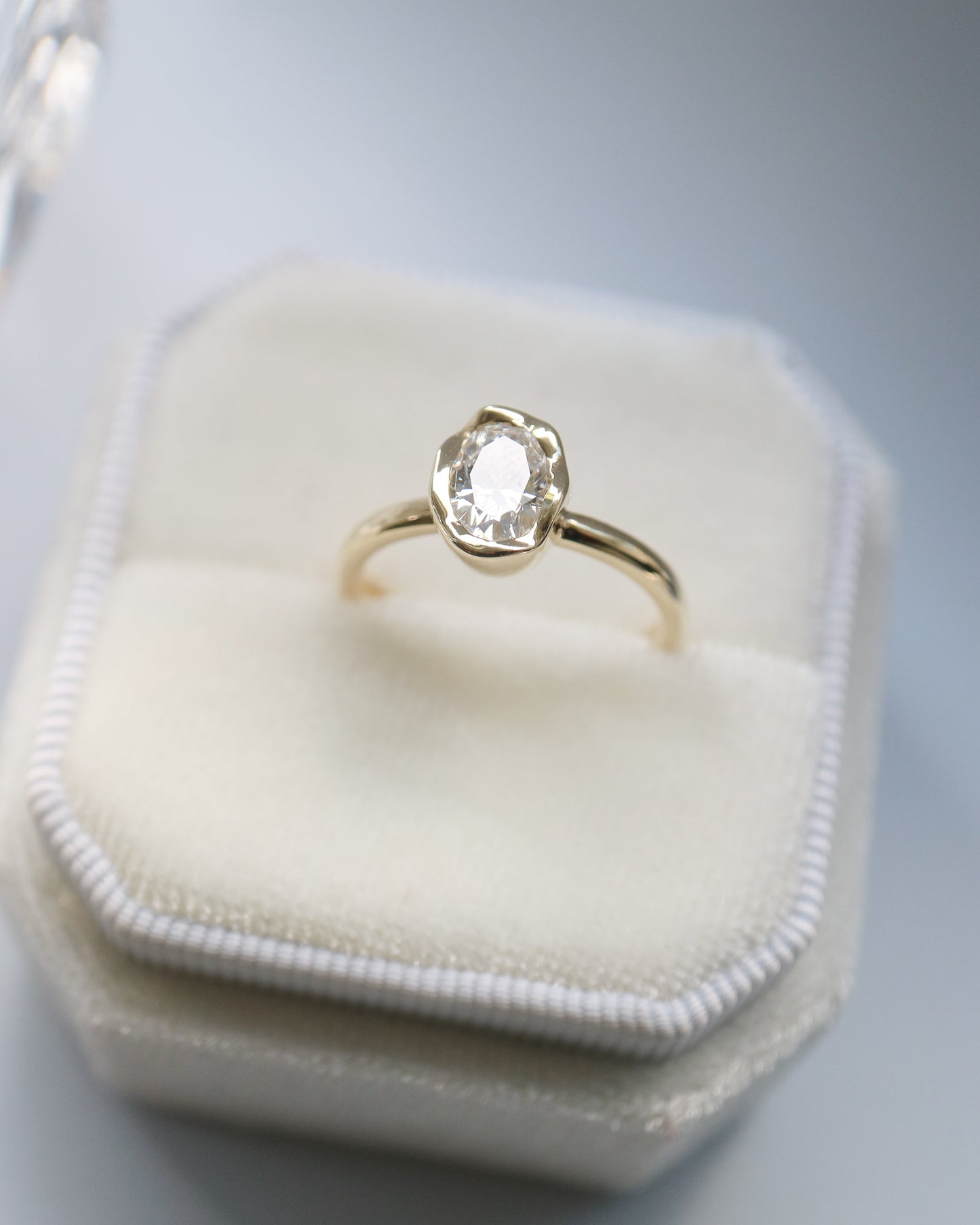 Gold ring with a diamond on a white hexagonal jewelry box against a gray background