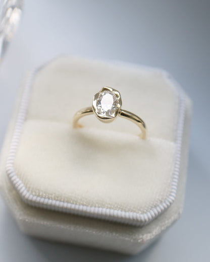 Gold ring with a diamond on a white hexagonal jewelry box against a gray background