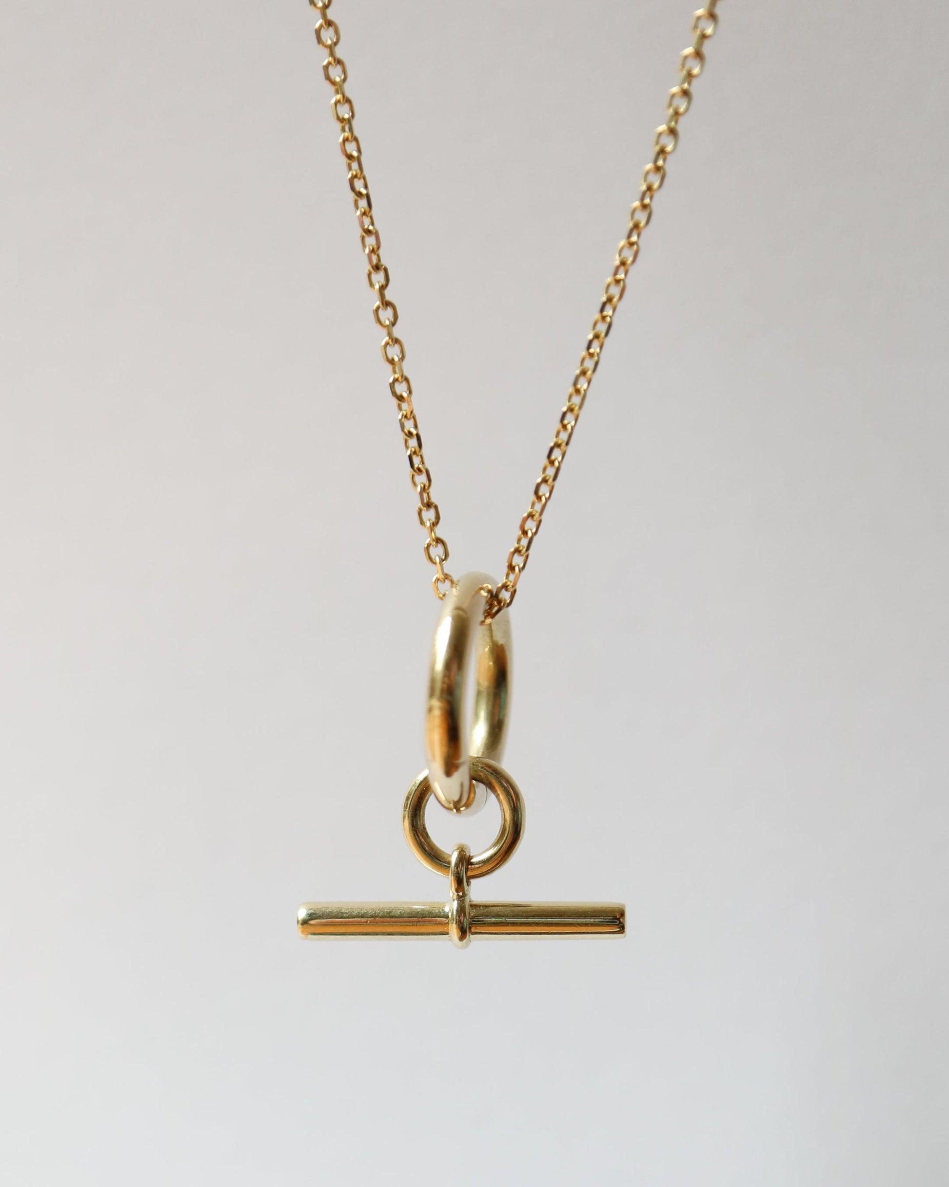Gold necklace with a T-bar pendant on a light gray background