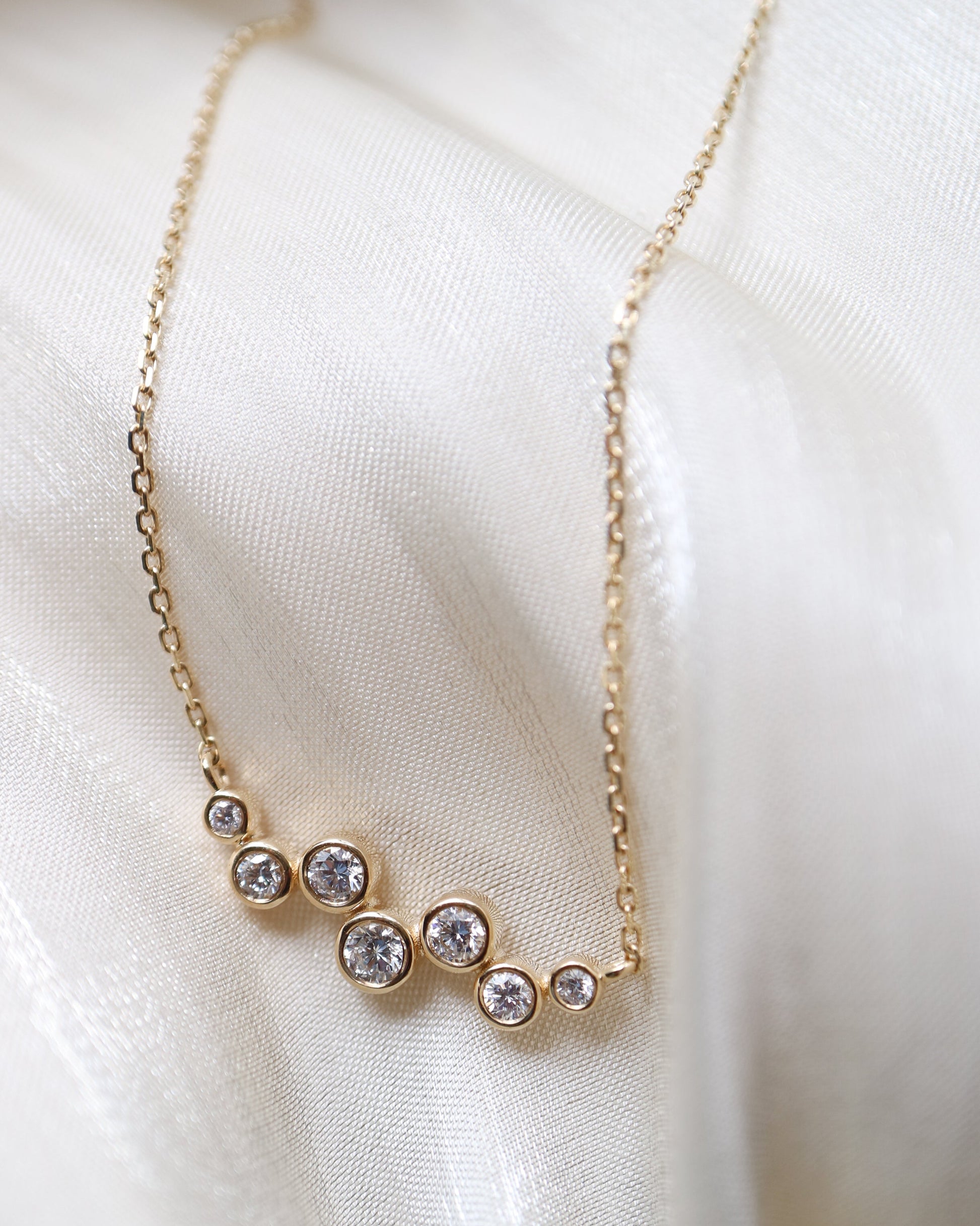 Delicate gold necklace with small diamonds on a soft white fabric background