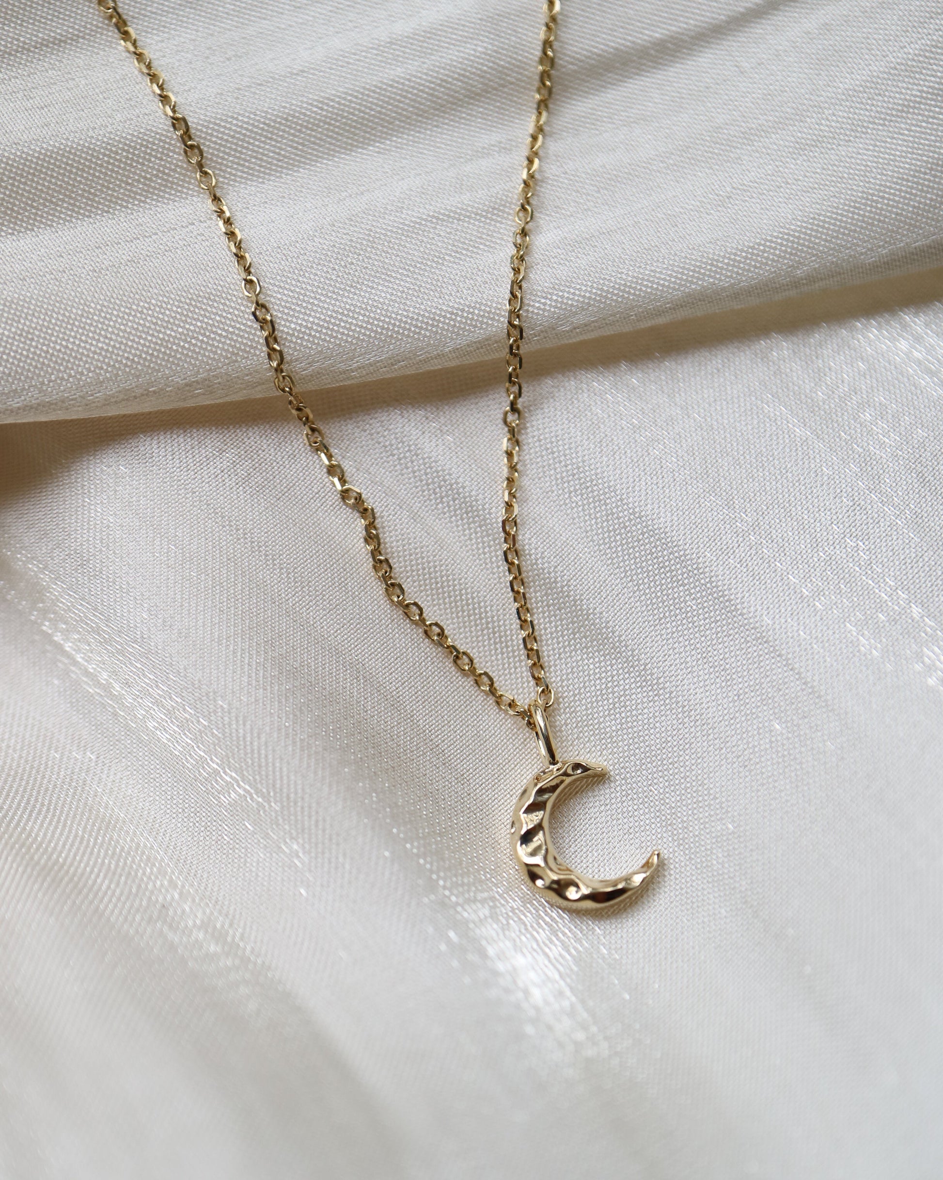 Gold necklace with a crescent moon pendant on a white fabric background