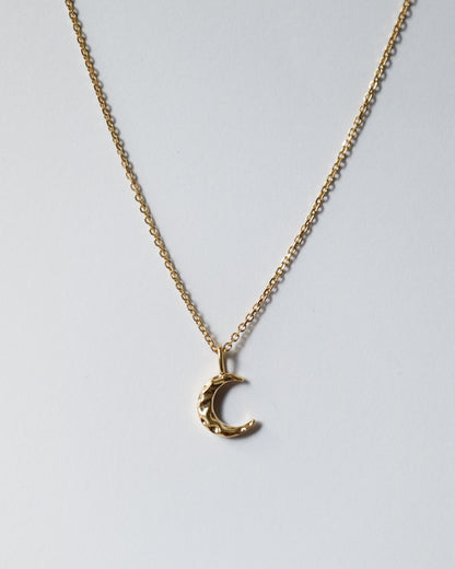 Gold crescent moon necklace on a light gray background