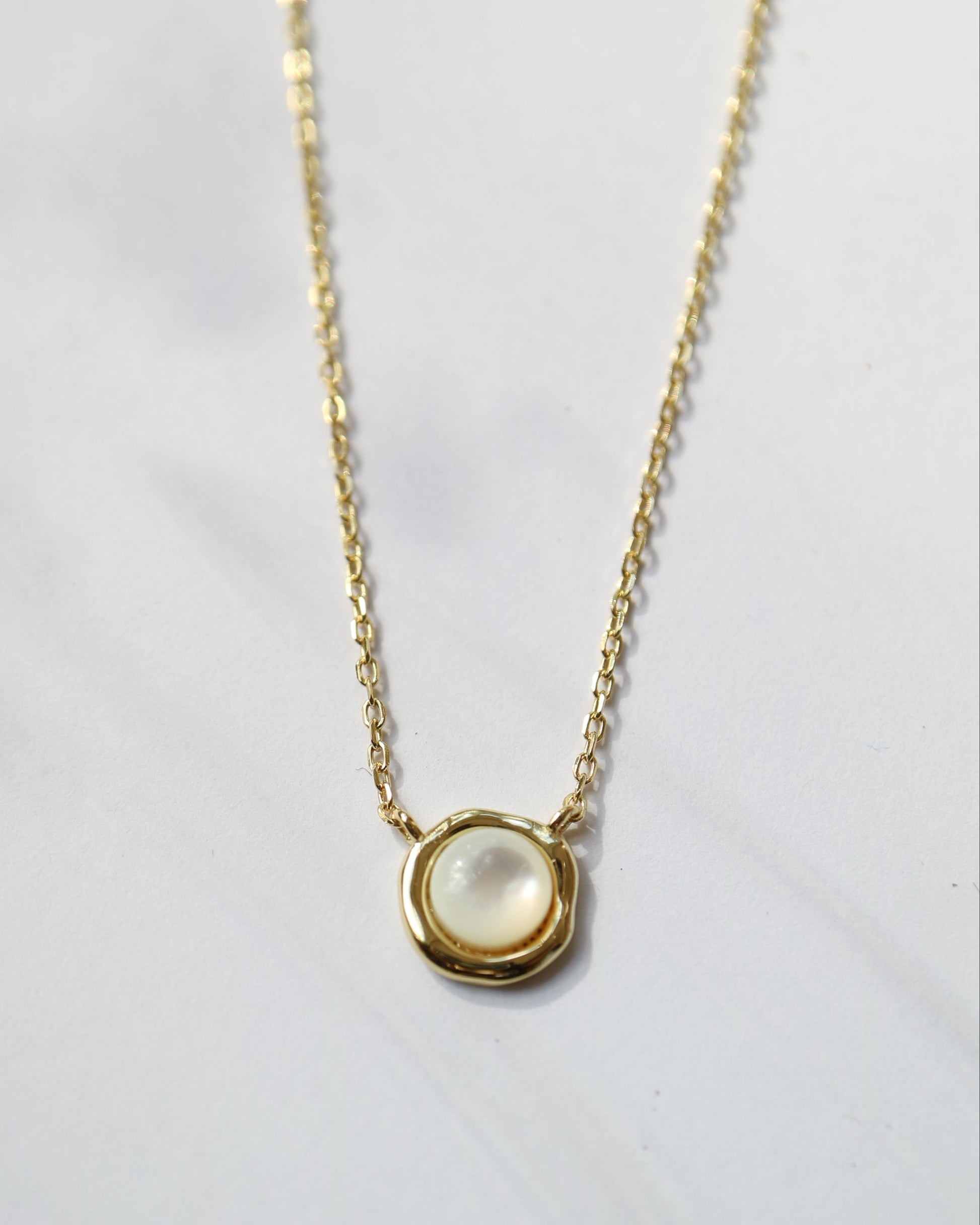 Gold necklace with a round pendant on a light gray background