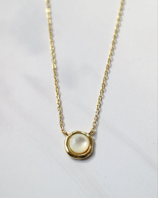 Gold necklace with a round pendant on a light gray background