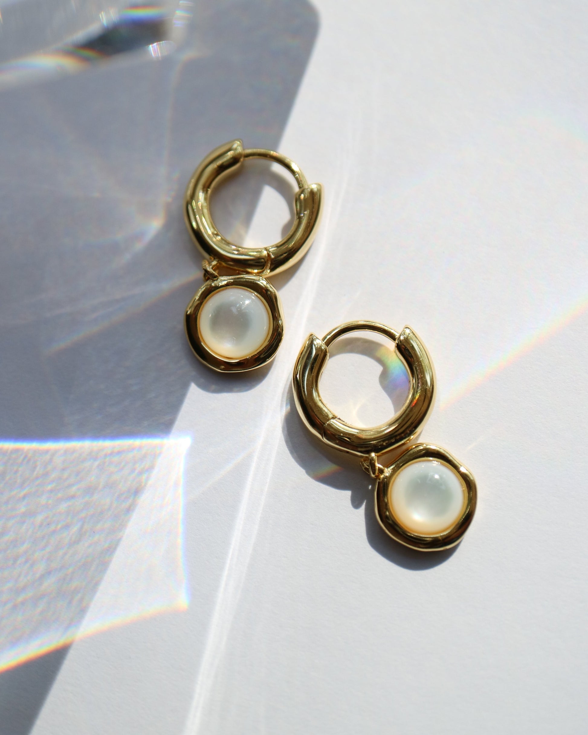Gold hoop earrings with a central gemstone on a light background