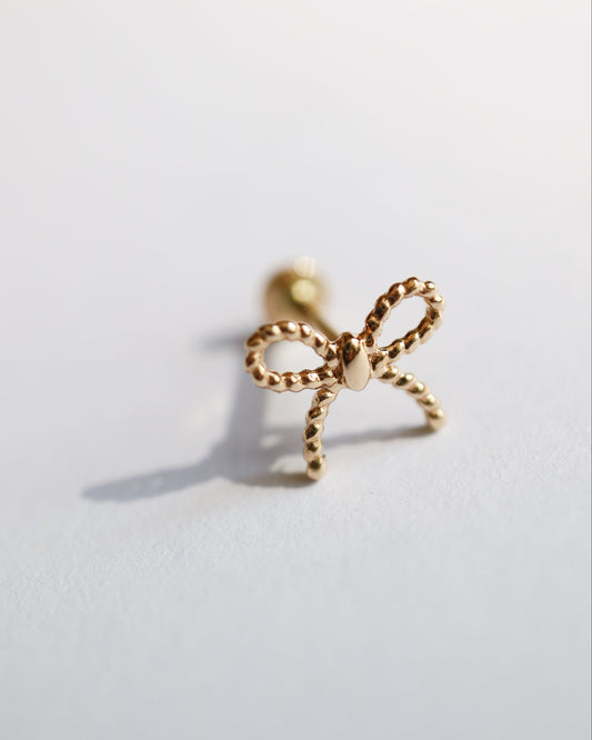 Gold bow-shaped earring on a light gray background
