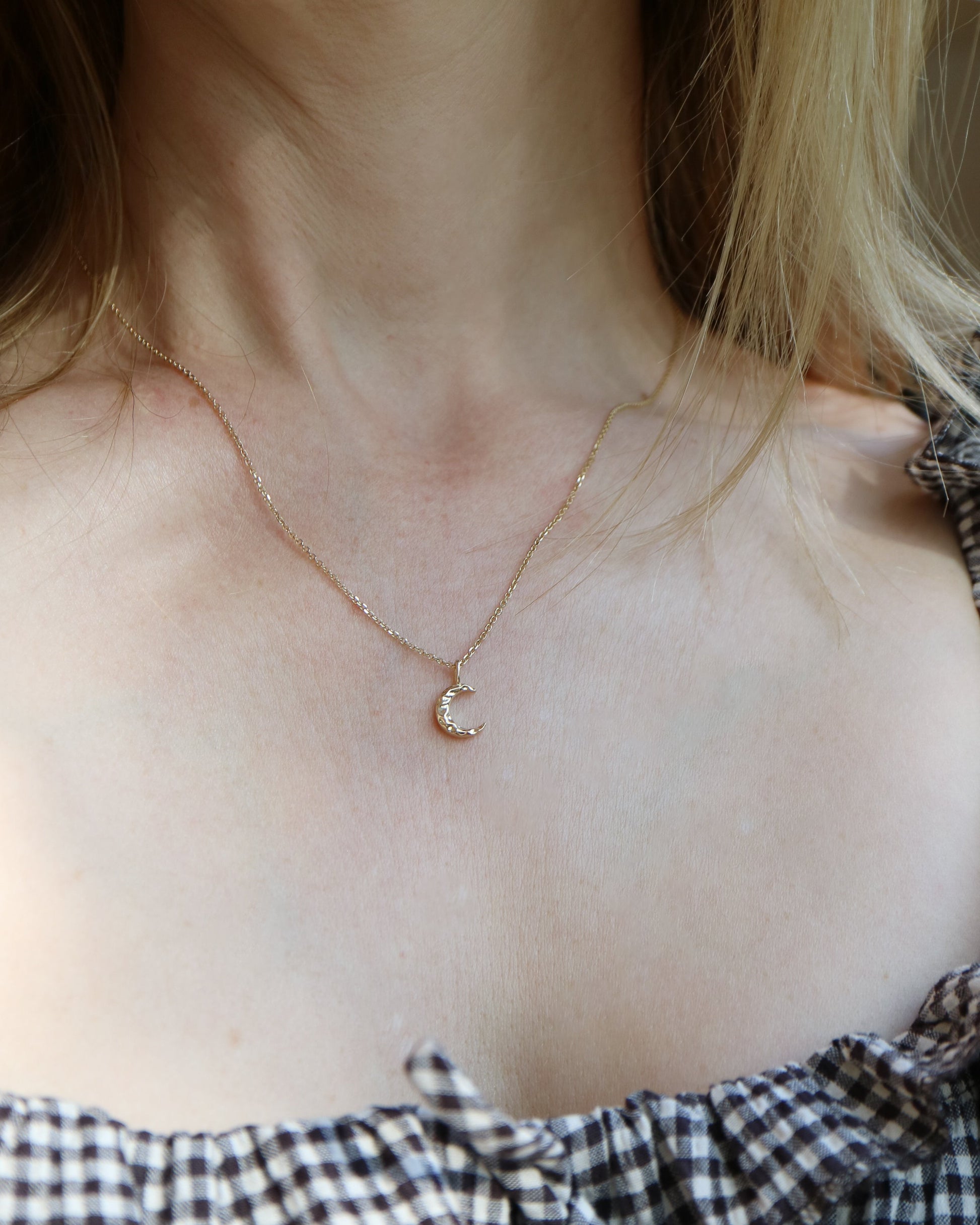 Necklace with a small round pendant worn by a person with checkered clothing.