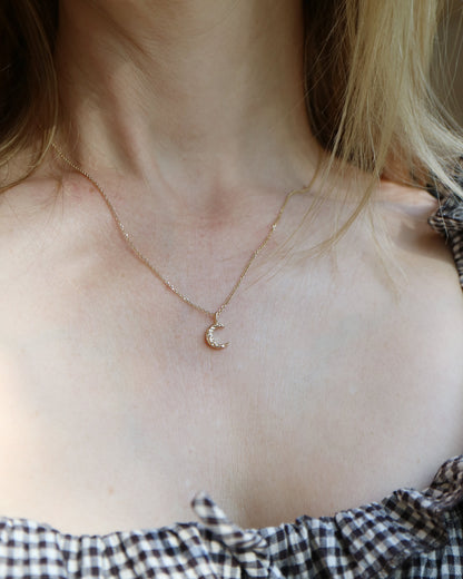 Necklace with a small round pendant worn by a person with checkered clothing.