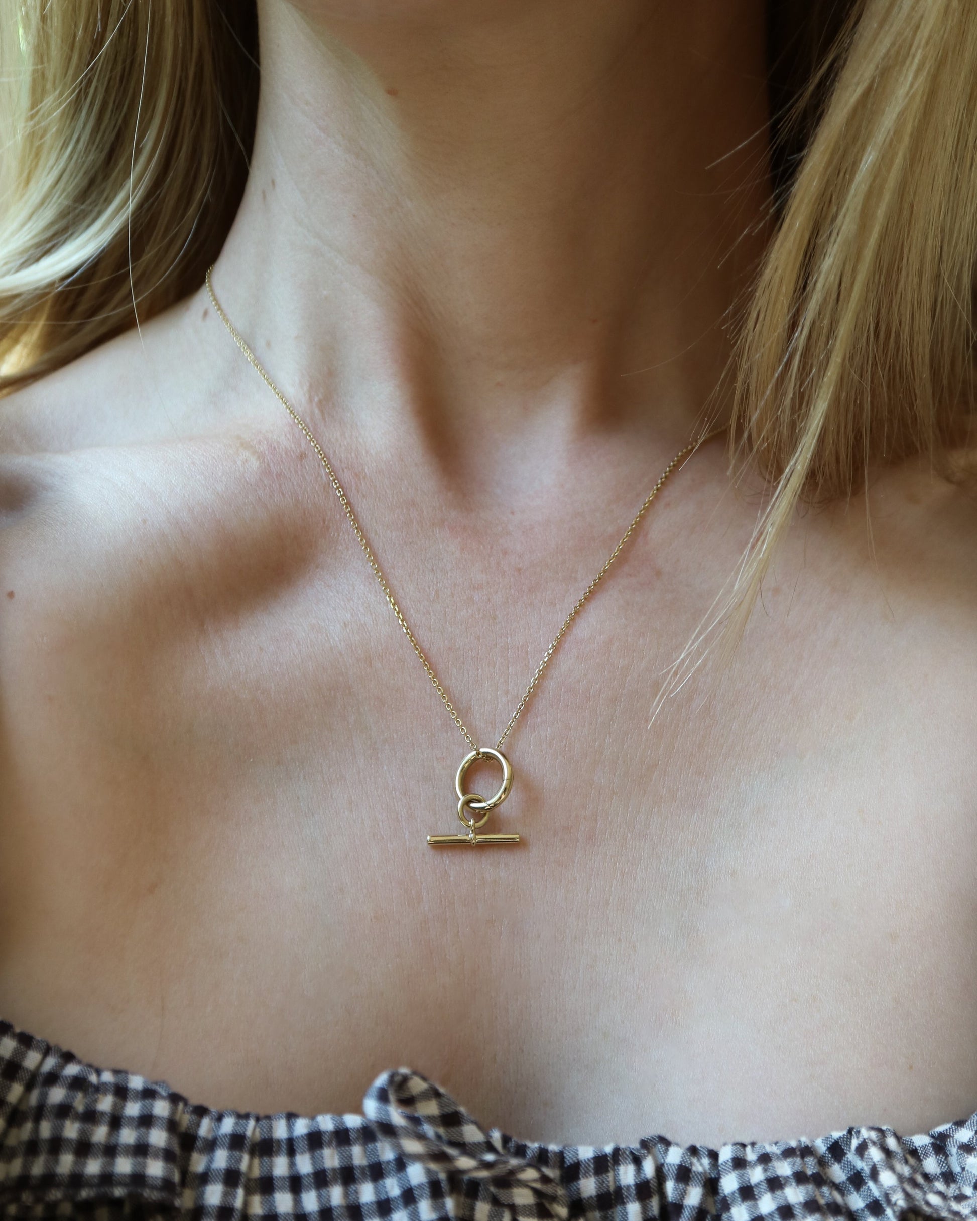 Close-up of a gold necklace with a pendant on a person wearing a checkered top.