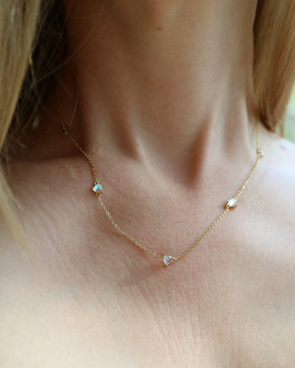 Close-up of a gold necklace with small heart-shaped pendants on a person wearing a checkered top.