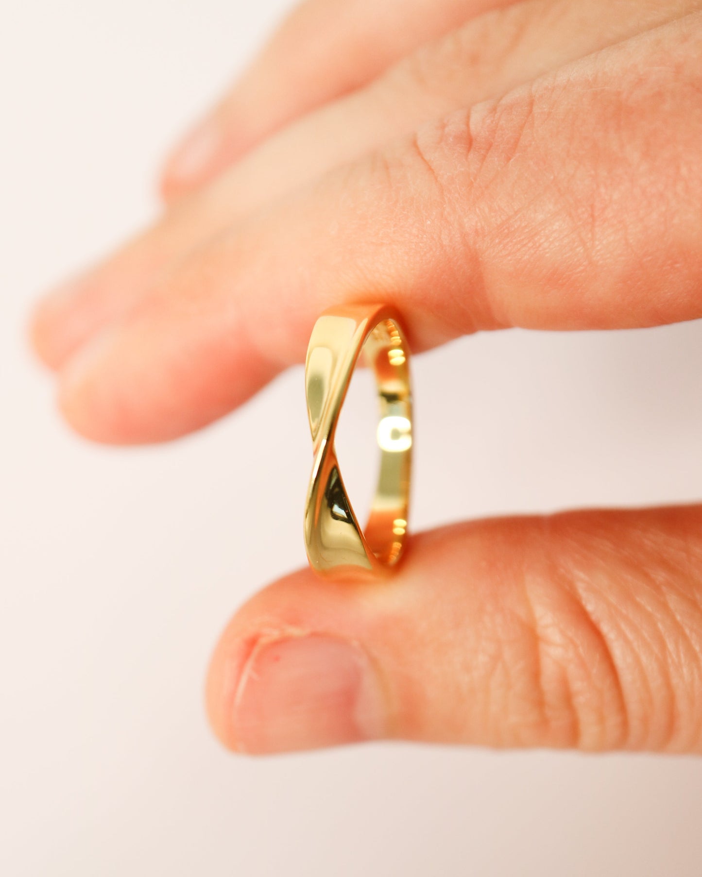 Gold ring being held between fingers on a white background