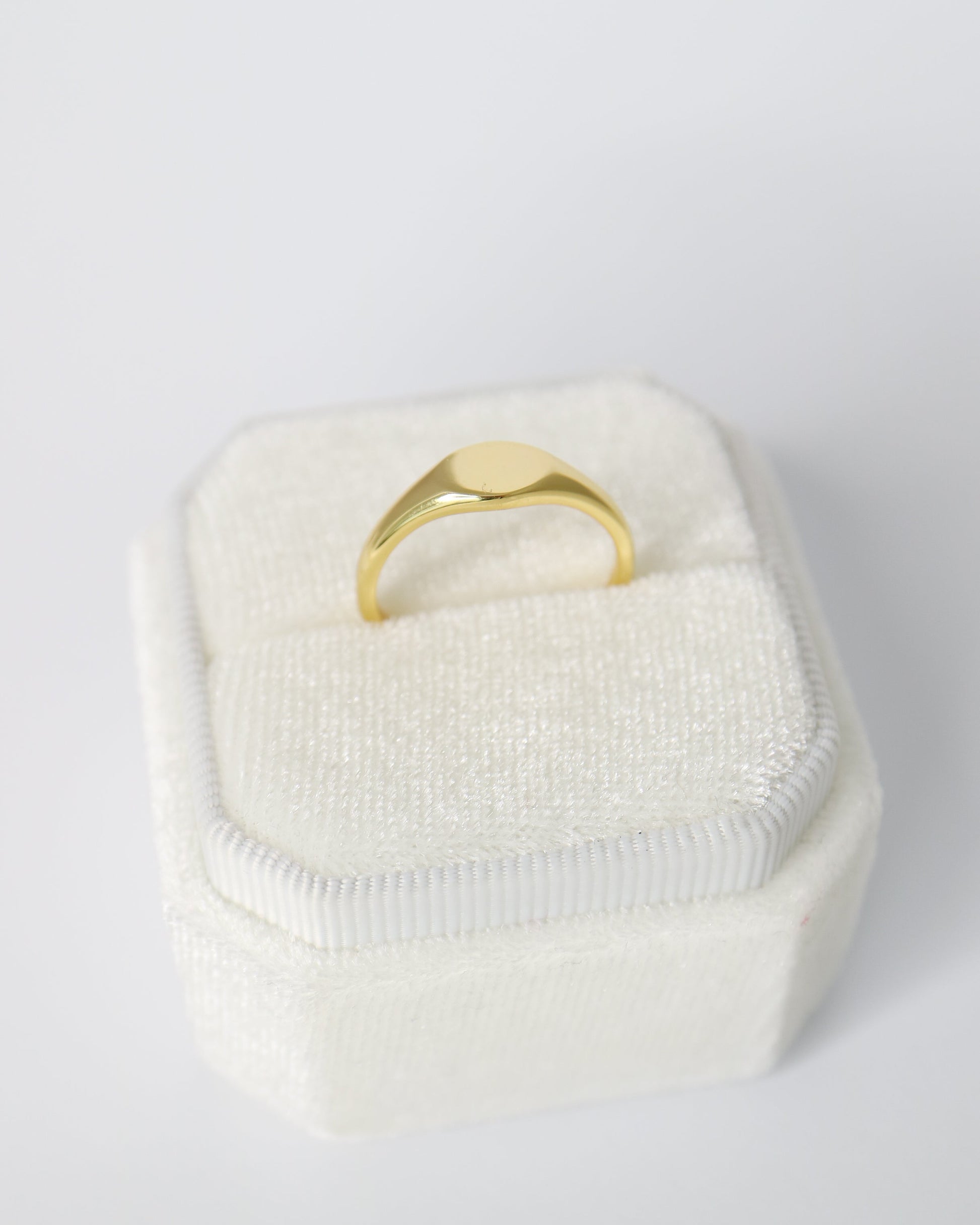 Gold ring in a white textured box on a light gray background