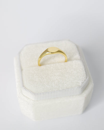 Gold ring in a white textured box on a light gray background