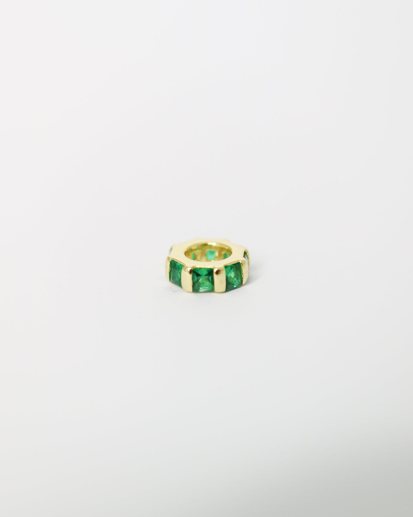 Gold ring with green gemstones on a light gray background