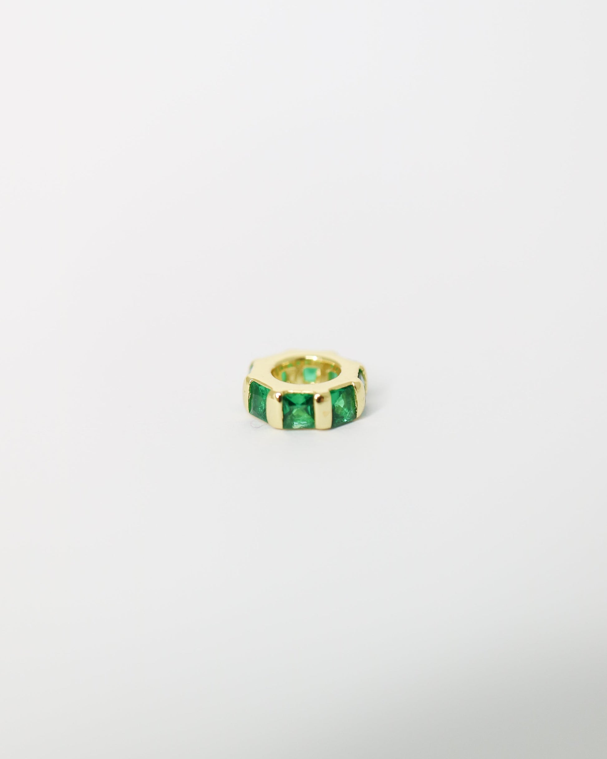 Gold ring with green gemstones on a light gray background